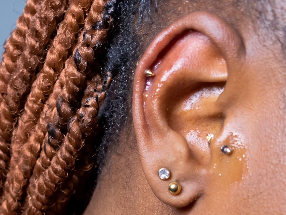 Close view of an ear with a gold spike stud in the upper ear, a crystal stud and a gold ball stud in the lobe, and a small crystal stud near the ear canal