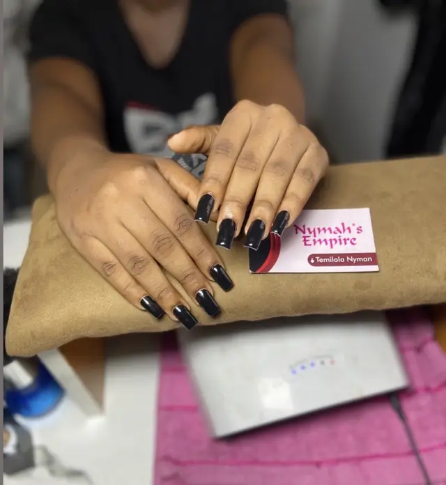 Glossy black square nails resting on a cushioned arm rest