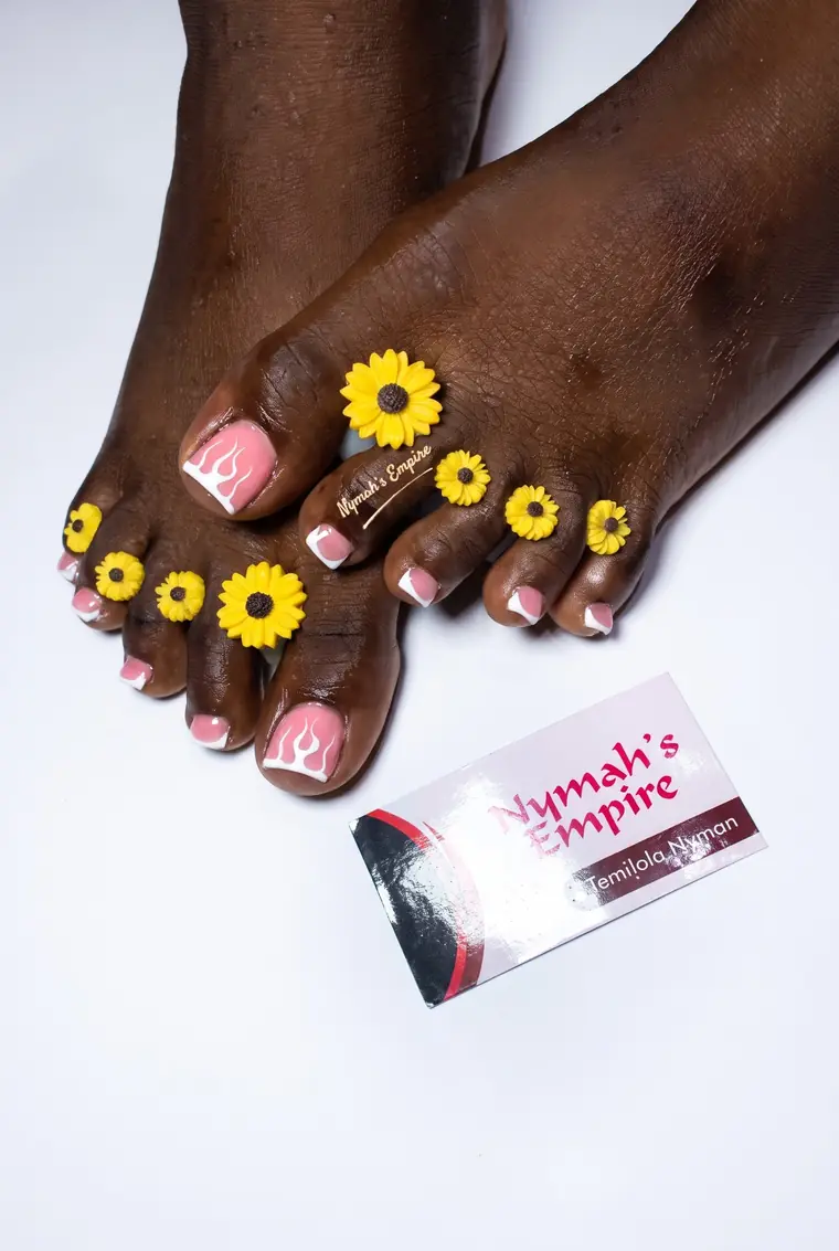 Pedicure with pink and white flame-style French tips and yellow sunflower accents between the toes